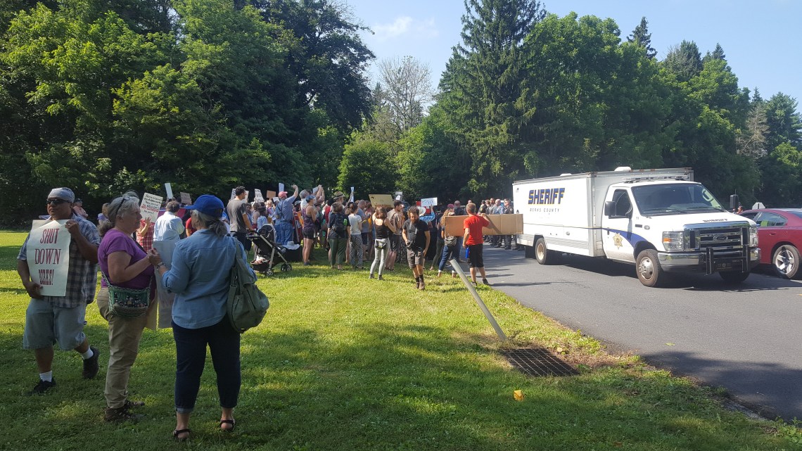 Dozens of people with signs saying "Shut Down Berks!" rally by a truck marked "Sheriff."