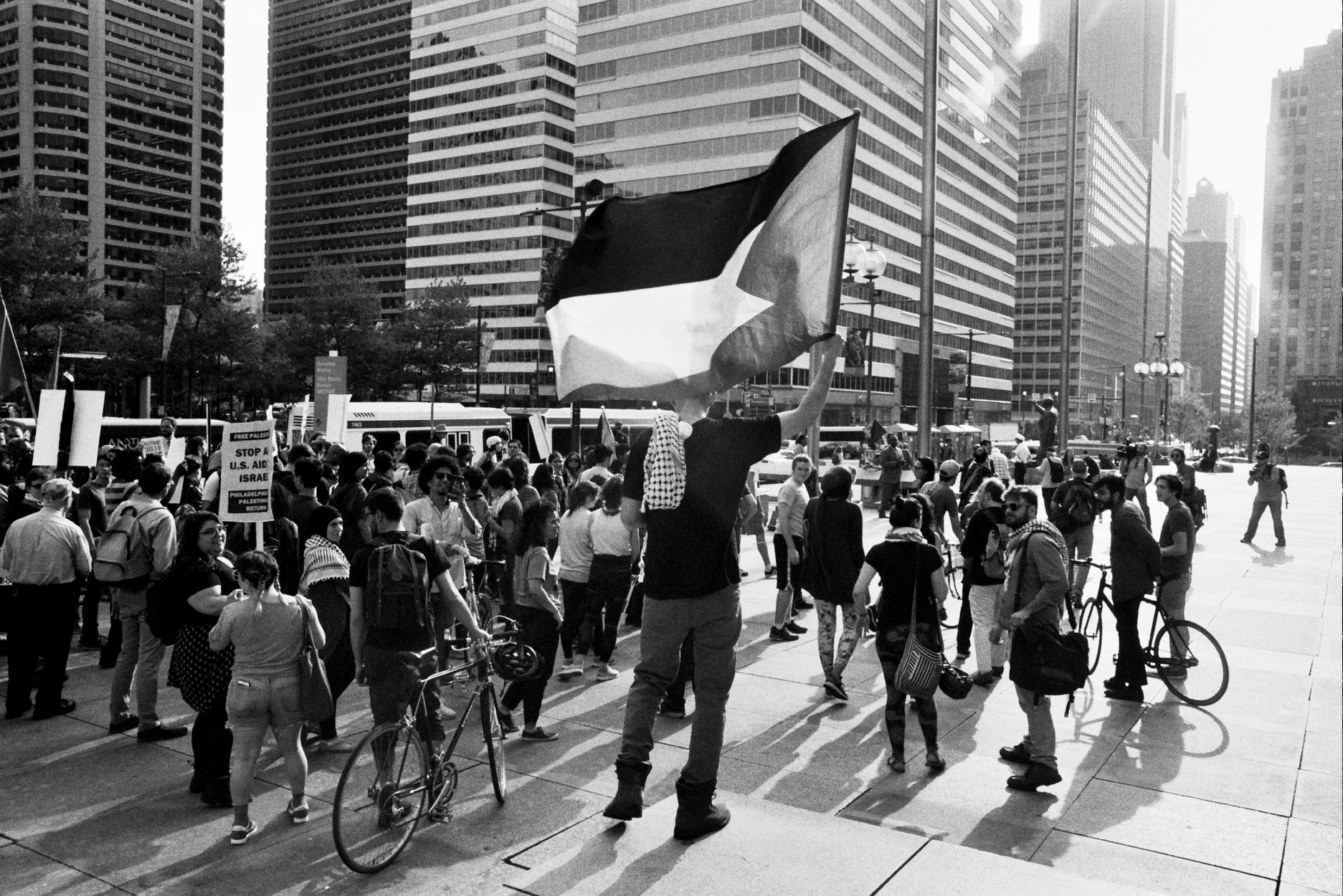 A person holds a Palestinian flag at the rally. Dozens of people gather outside City Hall.