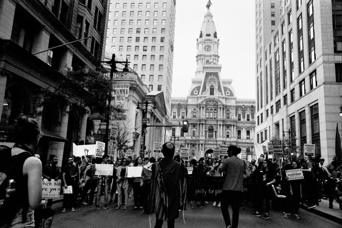 Dozens of people march in the street. Many are holding signs.