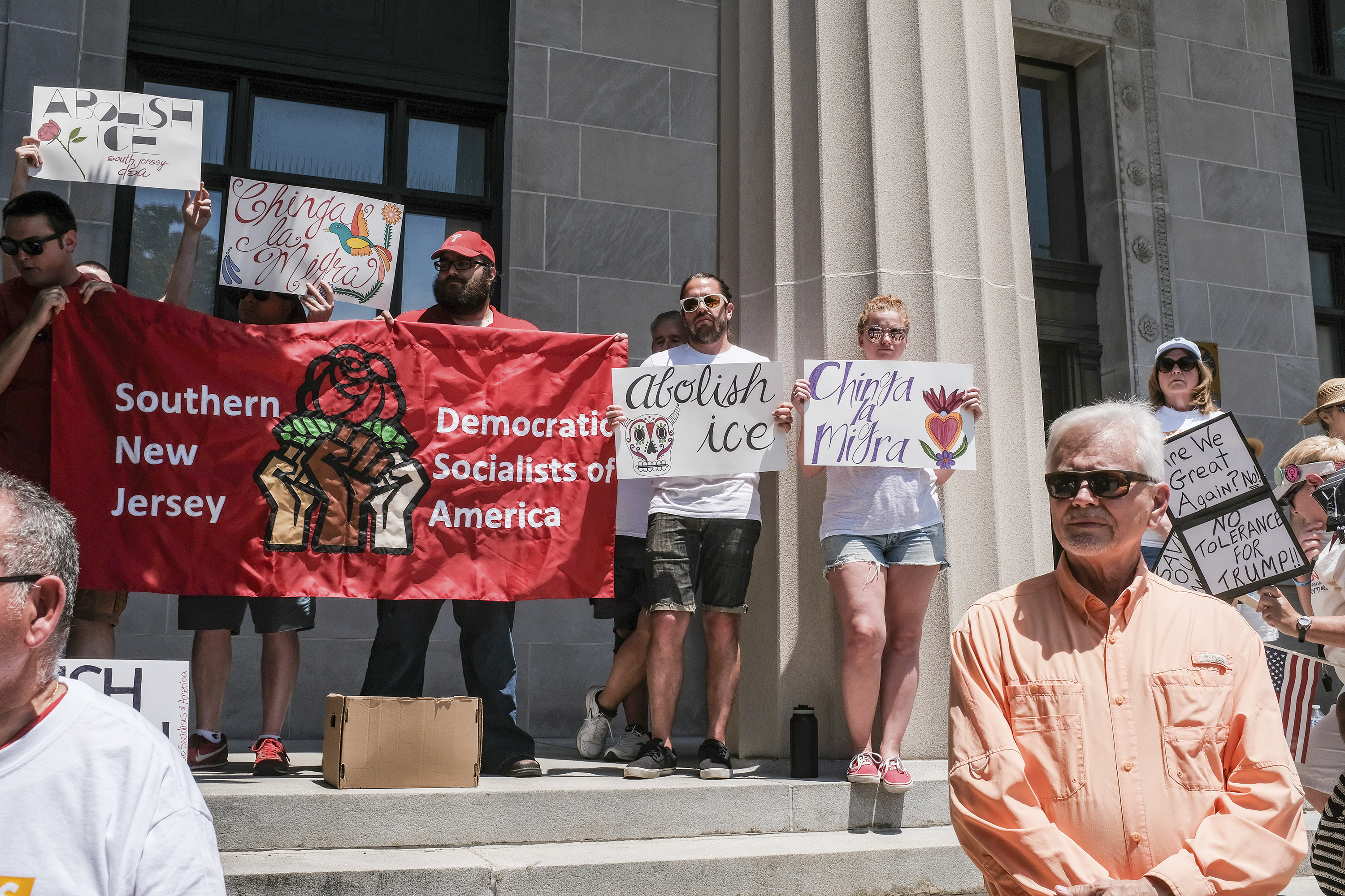 About a dozen activists stand holding signs that read "Chinga la Migra," and "Abolish ICE." They also hold a banner reading "Southern New Jersey Democratic Socialists of America."