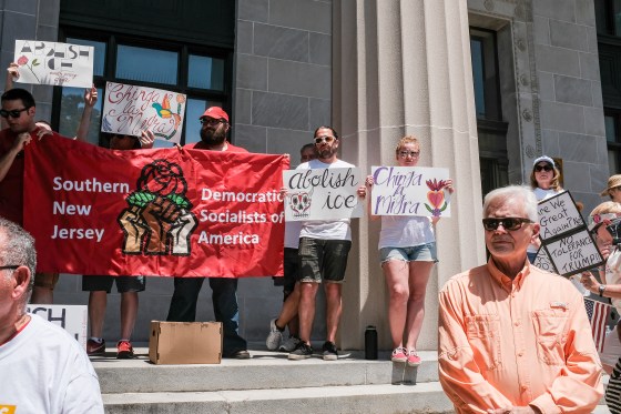 About a dozen activists stand holding signs that read "Chinga la Migra," and "Abolish ICE." They also hold a banner reading "Southern New Jersey Democratic Socialists of America."