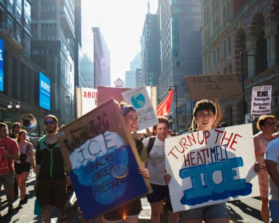 Protesters hold signs that read "Turn up the heat! Melt ICE" and "ICE cracks under pressure."